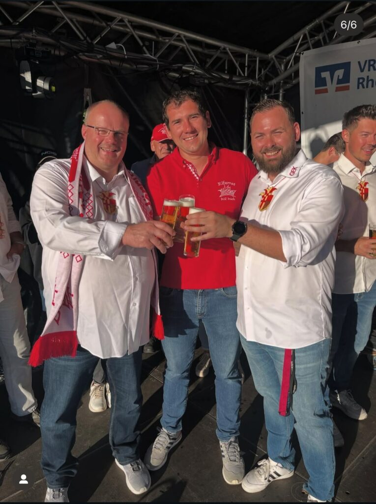 Mehrere Karnevalsteilnehmer feiern gemeinsam und stoßen während Rheinuferfest